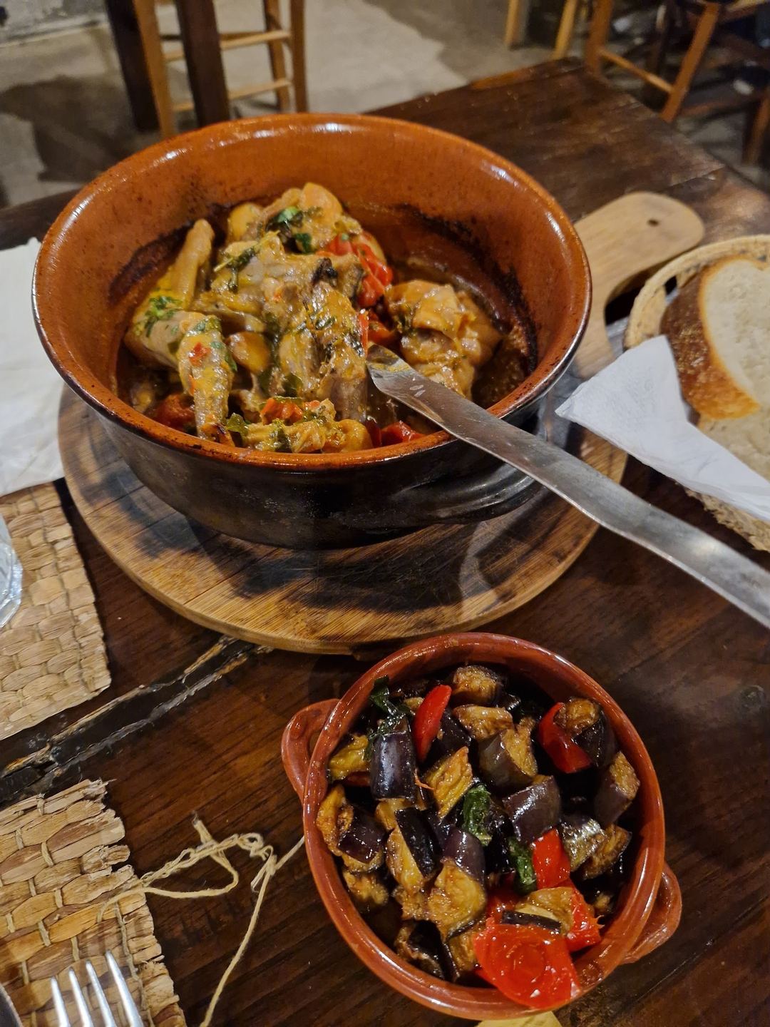 Traditional rustic dishes served in clay bowls featuring stewed meat with vegetables and roasted eggplant at an agriturismo restaurant.