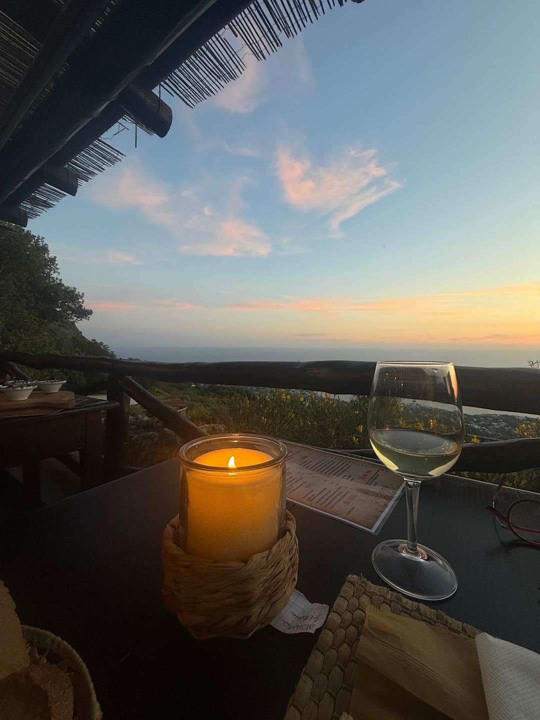 Sunset view from the terrace with a lit candle, wine glass, and expansive landscape vista at golden hour.